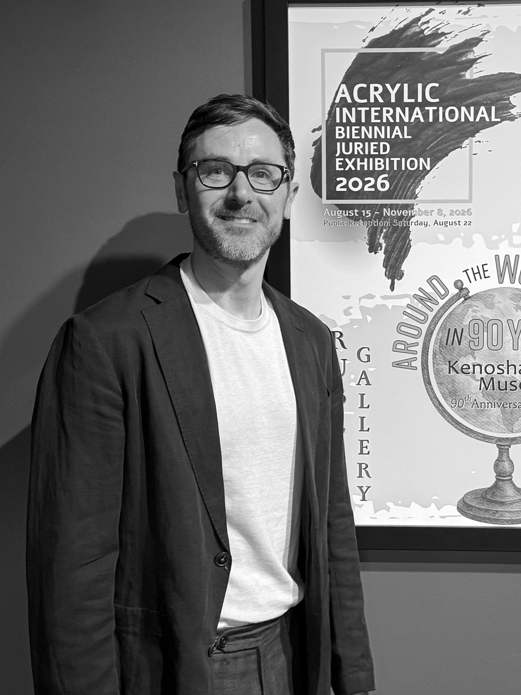 Alex Menenberg at the Kenosha Public Museum, beside the Acrylic International 2026 exhibition poster